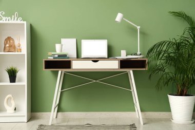 Laptop, lamba ve yeşil duvarın yanında kitapları olan modern işyeri