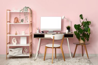 Oda pembe duvarın yanında dizüstü bilgisayarı ve kırtasiyesi olan modern işyeri