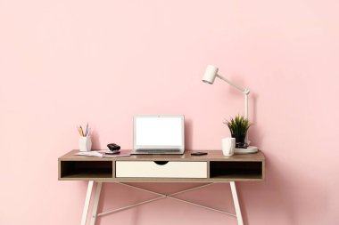 Oda pembe duvarın yanında dizüstü bilgisayarı ve kırtasiyesi olan modern işyeri