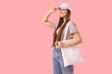 Pembe arka planda tekstil çantalı şapkalı genç bir kadın.