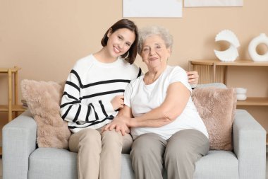 Genç hemşire ve yaşlı kadın evde kanepede kucaklaşıyorlar.