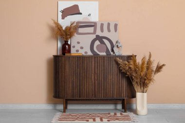 Çekmeceler, vazodaki otlar ve odadaki kahverengi duvarın yanındaki resimler.