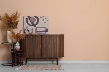 Çekmeceler, vazodaki otlar ve odadaki kahverengi duvarın yanındaki resim.