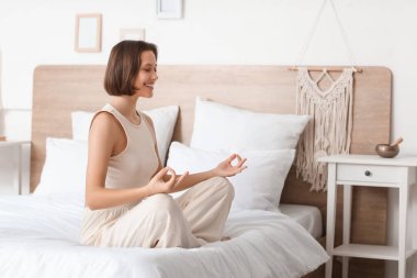 Güzel genç bir kadın evde yatakta meditasyon yapıyor.