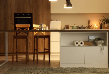 Akşam vakti mutfak masası, tezgahlar ve parlayan lambalar.