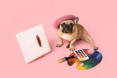 Pembe arka planda sanatçı malzemeleriyle bereli sevimli bir Fransız bulldog.