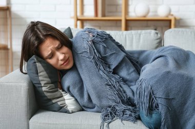 Oturma odasındaki kanepede ekoseli depresif genç kadın.