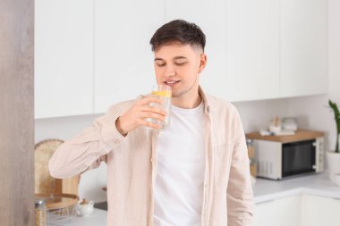 Genç adam mutfakta limonlu su içiyor.