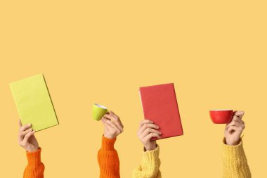 Sarı arka planda kitap ve kahve fincanları olan kadın eller.