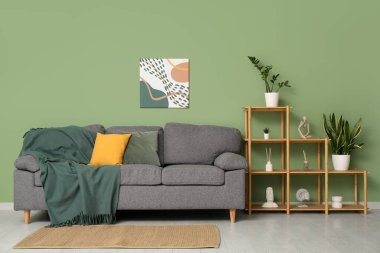 Yeşil duvarın yanında rahat kanepesi, boyası ve raf ünitesi olan şık bir oturma odası.