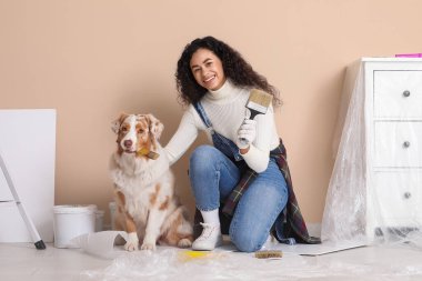 Fırçalı mutlu kadın Afro-Amerikan ressam ve yeni evdeki tamirat sırasında Avustralya çoban köpeği boyama duvarı.