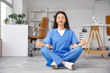 Genç bayan doktor klinikte yerde meditasyon yapıyor.