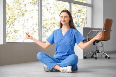 Genç bayan doktor klinikte yerde meditasyon yapıyor.