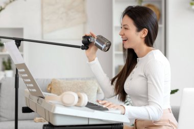 Evdeki kanepede mikrofonlu genç bir kadın sentezleyici çalıyor.