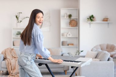 Mutlu genç kadın evde sentezleyici oynuyor.