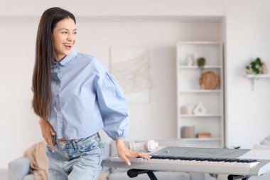 Mutlu genç kadın evde sentezleyici oynuyor.