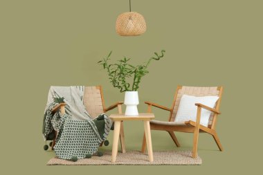 Vazoda bambu saplı masa, yeşil arka planda koltuklar ve lamba.