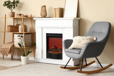 Şömineli oturma odası, raf ünitesi ve bej duvarın yanındaki gri sallanan sandalye.