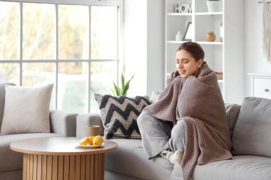 Evdeki masada ekose ve limonlu çay içen hasta genç bir kadın.