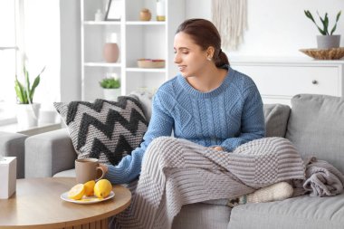 Gülümseyen genç bir kadın evdeki masadan bir bardak limon çayı alıyor.