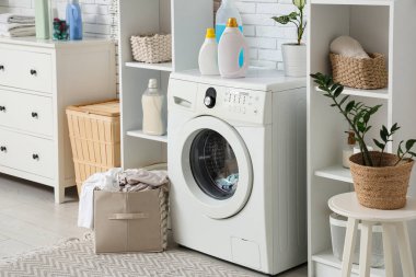 Çamaşır makinesi, deterjan şişeleri ve sepeti olan bir çamaşırhane.