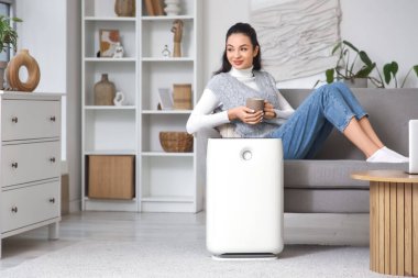 Evdeki kanepede bir fincan çay ve hava temizleyici ile genç bir kadın.