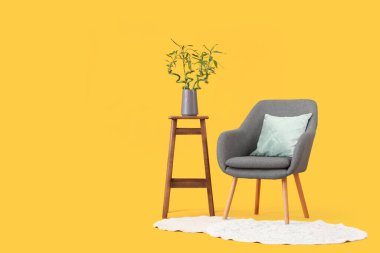 Vazoda bambu saplı masa, sarı arka planda koltuk ve halı.
