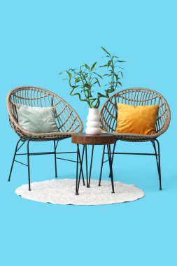 Vazoda bambu saplı masa, koltuklar ve mavi arka planda halı.