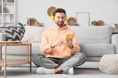 Evde cep telefonu kullanan kulaklıklı yakışıklı bir adam.