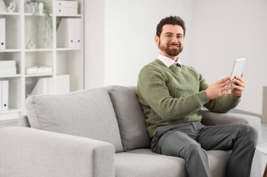 Ofisteki kanepede tablet bilgisayarla çalışan yakışıklı adam.