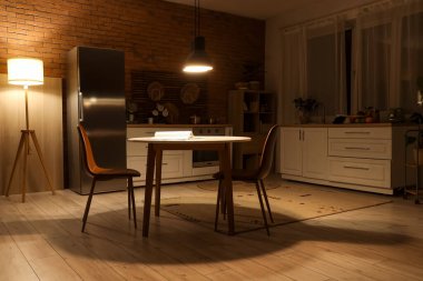 Karanlık mutfağın içinde tezgahlar, yemek masası ve geceleri parlayan lambalar var.