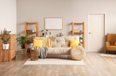 Aydınlık oturma odasının içinde bej kanepe, raf üniteleri ve bitkiler var.