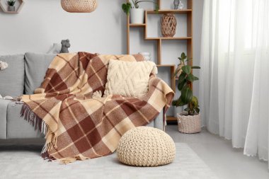 Modern odanın içinde yumuşak kareli battaniye, puf ve sehpa.