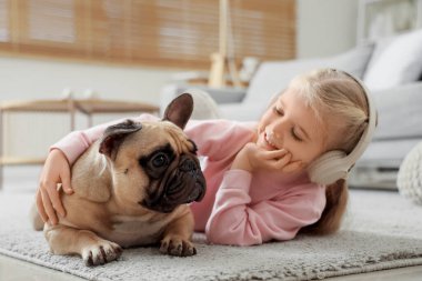 Kulaklıklı şirin, mutlu bir kız. Evde yerde yatan Fransız buldoguyla.