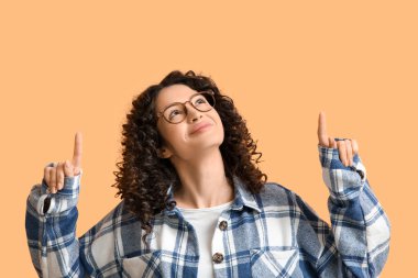 Genç bir kadın turuncu arka plandaki bir şeyi işaret ediyor.