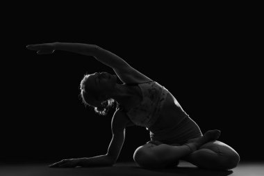 Siyah arka planda yoga yapan genç bir kadının silueti.