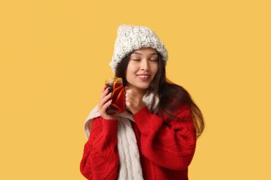 Sarı arka planda cam bir kavanoz sıcak şarapla güzel, mutlu, Asyalı bir kadın.