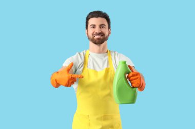 Önlüklü yakışıklı adam mavi arka planda çamaşır deterjanı gösteriyor.