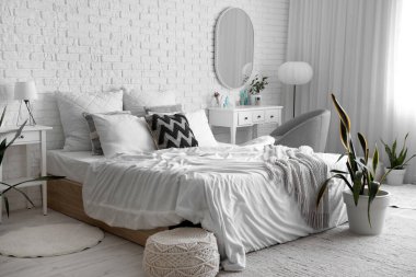 Yatak odasının içinde yatak odası, ayna ve kozmetik ürünler beyaz tuğlaların yanında makyaj masasında.