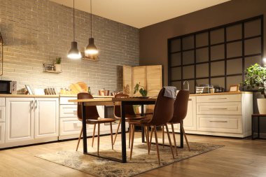 Mutfağın içinde tezgahlar, yemek masası ve akşam lambaları var.