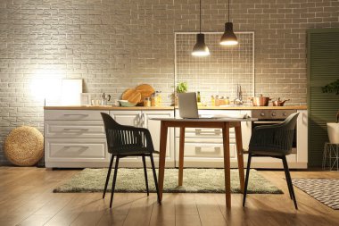 Karanlık mutfağın içinde tezgahlar, yemek masası ve akşamları parlayan lambalar.