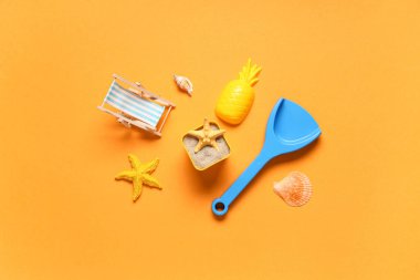 Plaj oyuncağı kalıbı, kum, dekoratif iskemle, deniz kabuğu, oyuncak kürek ve turuncu arka planda deniz yıldızları.