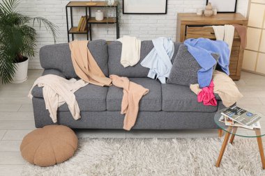 Gri kanepesi, kahve masası ve dağınık giysileri olan dağınık bir oturma odası.