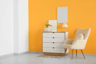 Koltuklu beyaz çekmeceler ve sarı duvarlı boş posterler.