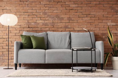 Oturma odasının içinde gri kanepe, masa ve parlayan lamba var.