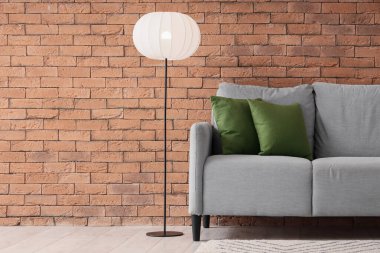 Yastıklı gri kanepe ve tuğla duvarın yanında parlayan lamba.