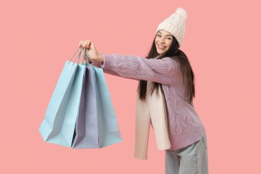 Pembe arka planda alışveriş torbaları olan kalın giysili güzel bir kadın.