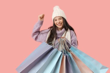 Pembe arka planda alışveriş torbaları olan kalın giysili güzel bir kadın.