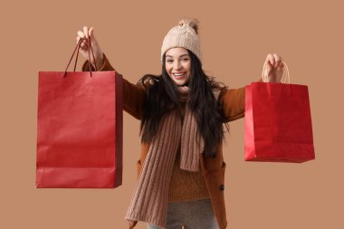 Kahverengi arka planda alışveriş torbaları olan kalın elbiseli güzel bir kadın.