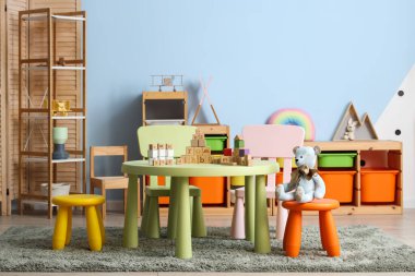 Çocuk oyun odasının içinde masa, raf üniteleri ve farklı oyuncaklar var.